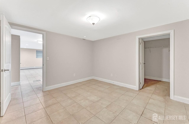 unfurnished bedroom featuring a baseboard radiator, a walk in closet, light tile patterned flooring, and a closet