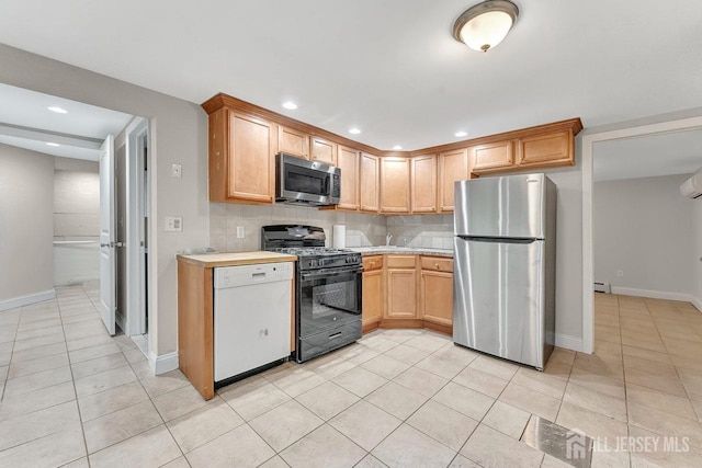 kitchen featuring light tile patterned flooring, light brown cabinets, baseboard heating, stainless steel appliances, and backsplash