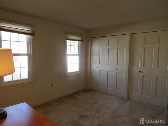 unfurnished bedroom featuring carpet floors, visible vents, baseboards, and multiple closets