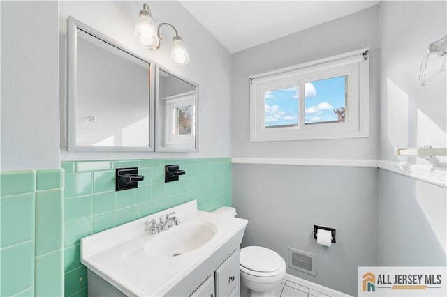 bathroom featuring toilet, vanity, and tile walls