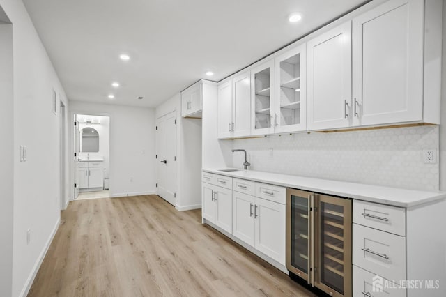 kitchen with beverage cooler, white cabinets, decorative backsplash, glass insert cabinets, and light countertops