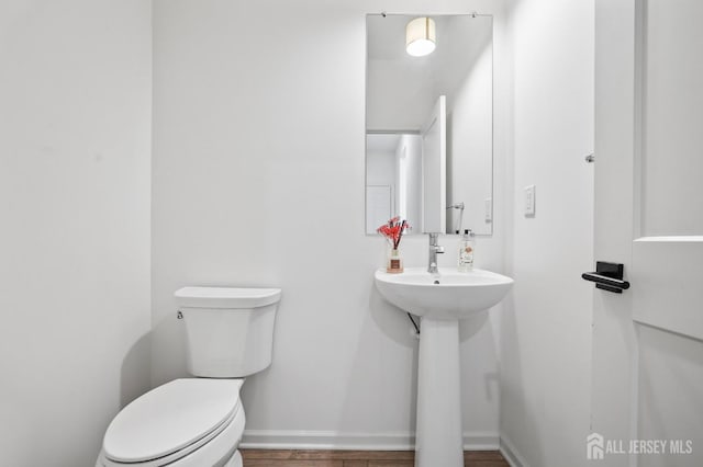 half bathroom with toilet, baseboards, and wood finished floors