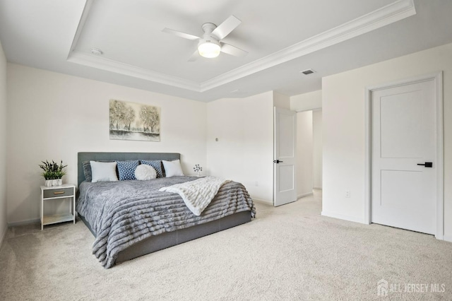 bedroom with ornamental molding, a tray ceiling, light colored carpet, and a ceiling fan