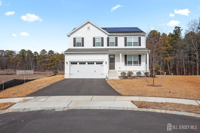 traditional home featuring an attached garage, roof mounted solar panels, fence, and aphalt driveway