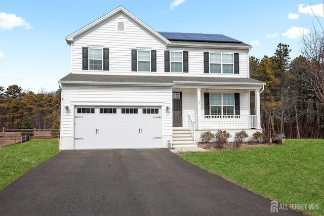 traditional-style house with an attached garage, covered porch, driveway, roof mounted solar panels, and a front yard