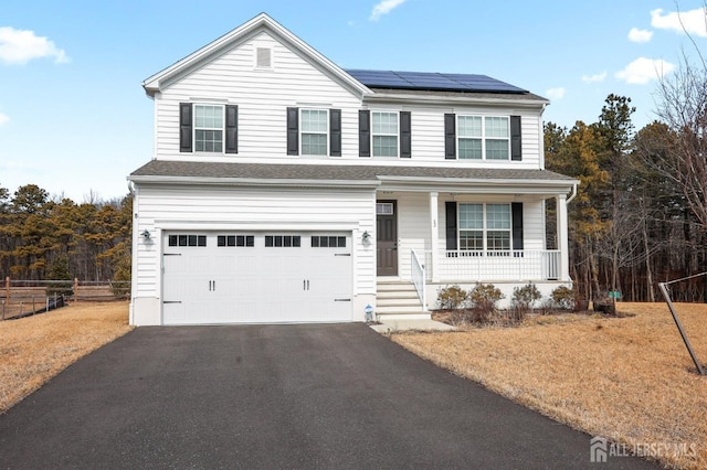 traditional home featuring aphalt driveway, solar panels, covered porch, an attached garage, and fence