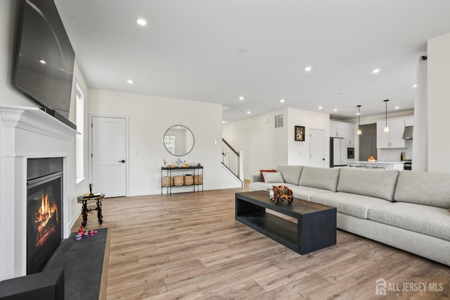 living area with visible vents, a glass covered fireplace, stairway, light wood-style floors, and recessed lighting