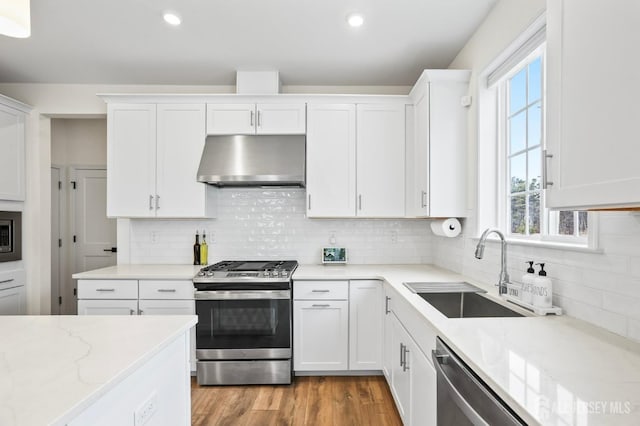 kitchen with light stone counters, a sink, white cabinetry, ventilation hood, and appliances with stainless steel finishes