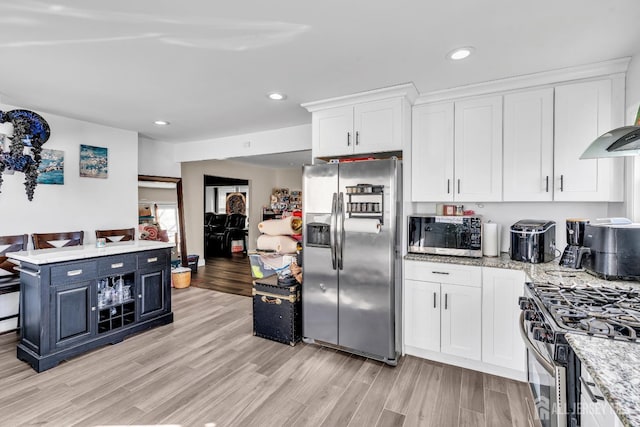 kitchen with wall chimney range hood, light hardwood / wood-style flooring, stainless steel appliances, light stone countertops, and white cabinets