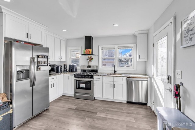 kitchen with appliances with stainless steel finishes, white cabinetry, sink, light stone counters, and wall chimney exhaust hood