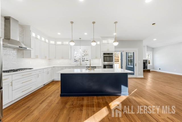 kitchen with a kitchen island, double oven, wall chimney exhaust hood, light countertops, and glass insert cabinets