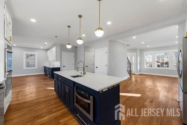 kitchen featuring white cabinets, wood finished floors, blue cabinets, light countertops, and a sink