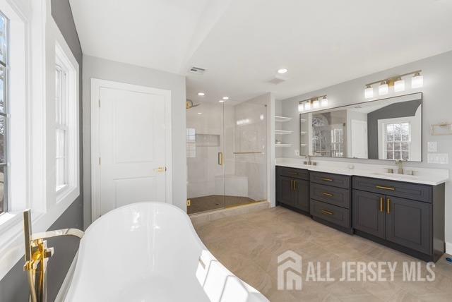 bathroom with a stall shower, a soaking tub, a sink, and double vanity