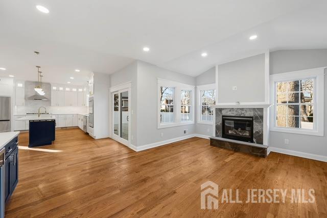 unfurnished living room with light wood finished floors, recessed lighting, vaulted ceiling, and a high end fireplace