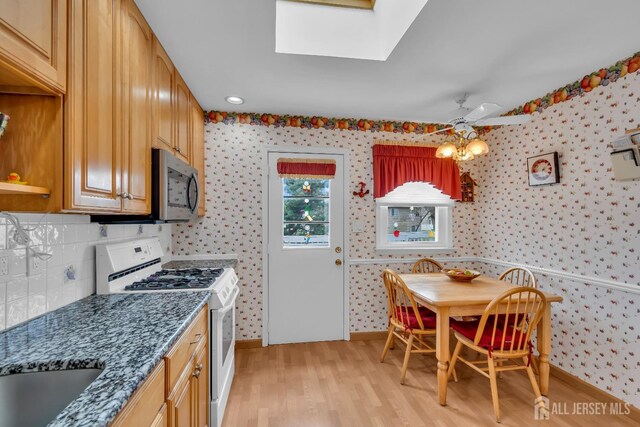 423 Brentwood Dr, Piscataway, NJ 08854 - kitchen with stainless steel microwave, white gas range oven, wallpapered walls, a skylight, and light wood-style flooring