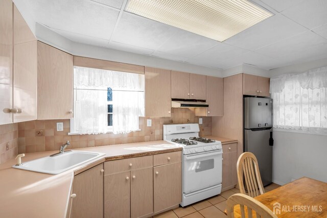 kitchen with stainless steel fridge, light tile patterned floors, decorative backsplash, white gas stove, and sink