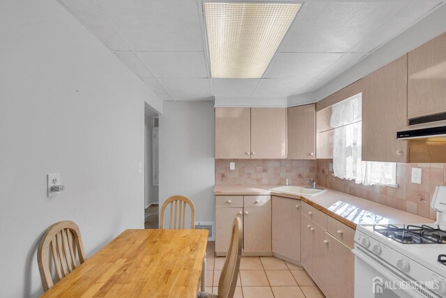 kitchen with white gas range, light brown cabinetry, light tile patterned floors, decorative backsplash, and sink