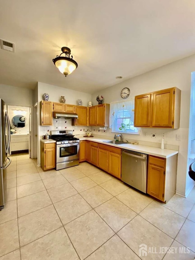 57 Yorktown Rd, South Brunswick, NJ 08852 - kitchen with stainless steel appliances, under cabinet range hood, light countertops, light tile patterned flooring, and brown cabinetry