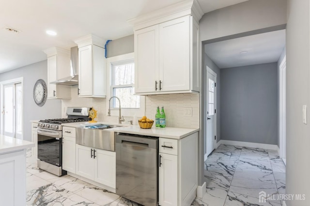 kitchen featuring marble finish floor, wall chimney range hood, white cabinetry, tasteful backsplash, and appliances with stainless steel finishes