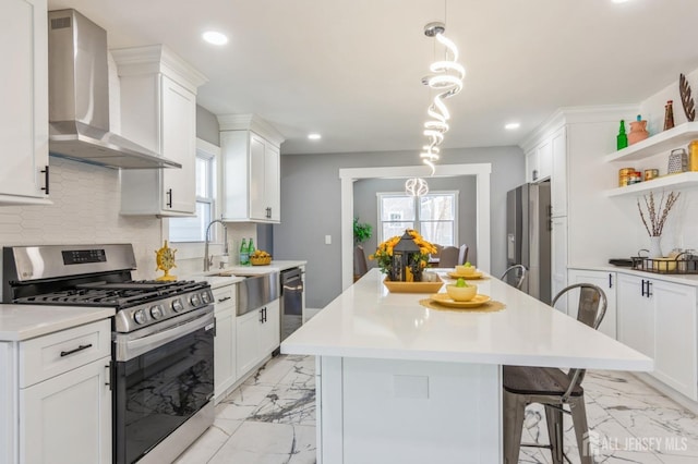 kitchen with a sink, stainless steel appliances, wall chimney exhaust hood, and marble finish floor