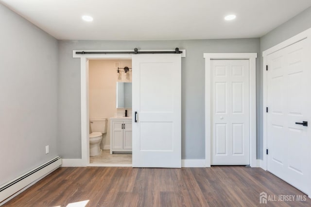unfurnished bedroom with recessed lighting, a baseboard heating unit, a barn door, and dark wood finished floors