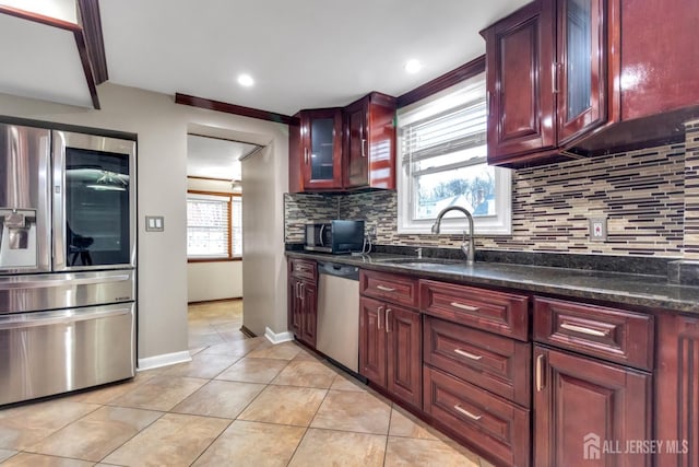 kitchen featuring dark stone countertops, sink, tasteful backsplash, light tile patterned floors, and appliances with stainless steel finishes