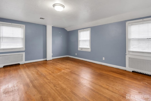 spare room with light wood-type flooring, radiator, and vaulted ceiling