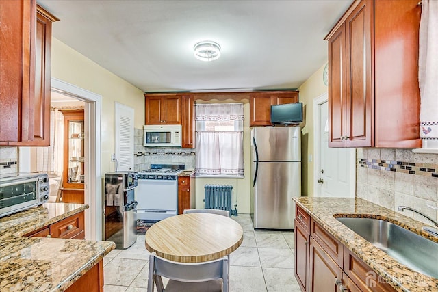 kitchen with sink, light stone counters, radiator heating unit, white appliances, and backsplash