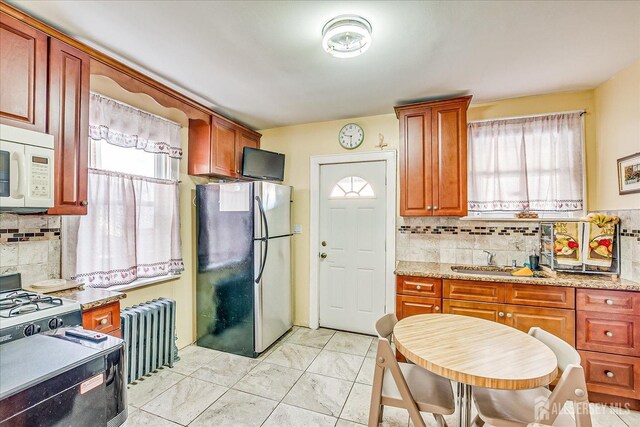 kitchen with sink, light stone counters, stainless steel refrigerator, radiator heating unit, and decorative backsplash