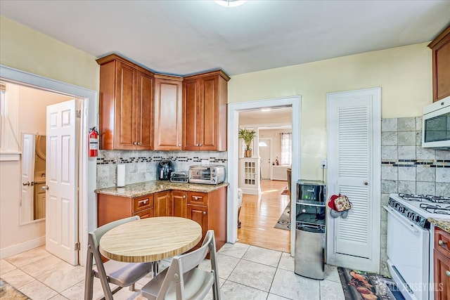 kitchen featuring tasteful backsplash, light tile patterned floors, light stone counters, and gas range gas stove