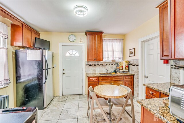 kitchen featuring stainless steel refrigerator, light stone countertops, sink, and backsplash