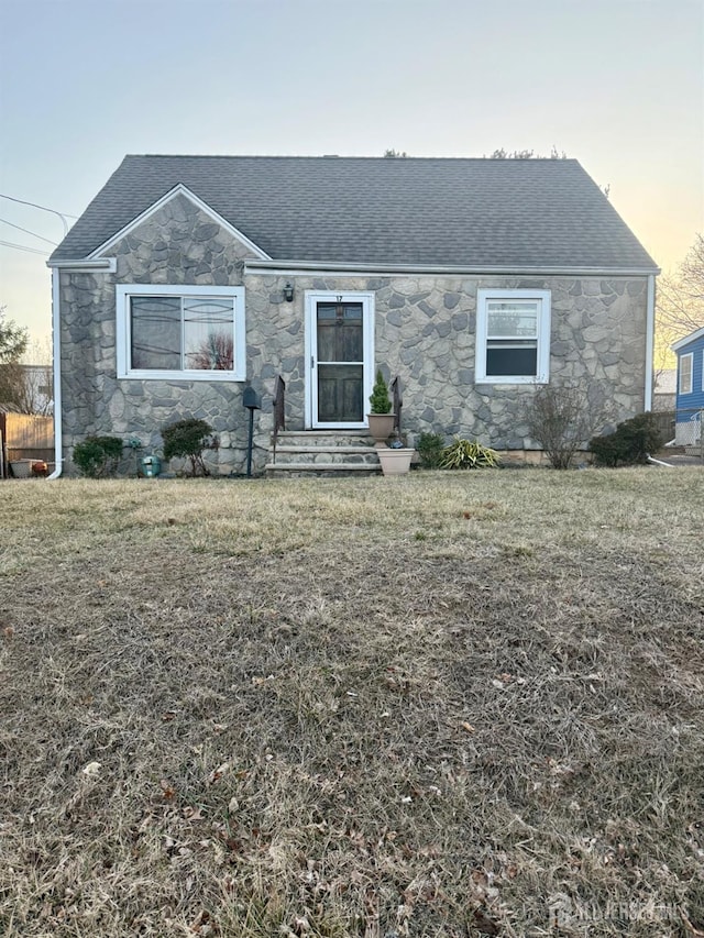 view of front of home featuring stone siding, a shingled roof, and a front lawn