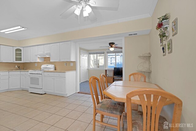 kitchen with sink, light tile patterned floors, gas range gas stove, ornamental molding, and white cabinets