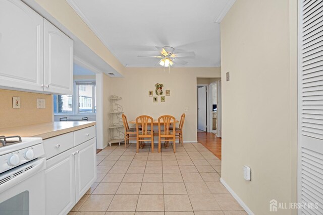 kitchen with light tile patterned floors, crown molding, white gas range oven, ceiling fan, and white cabinets