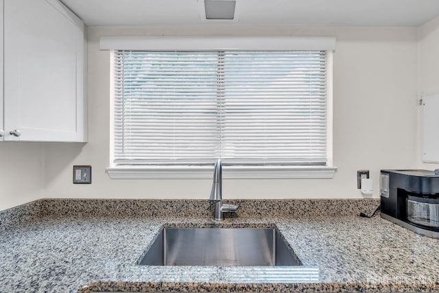 interior details featuring white cabinetry, light stone counters, and a sink