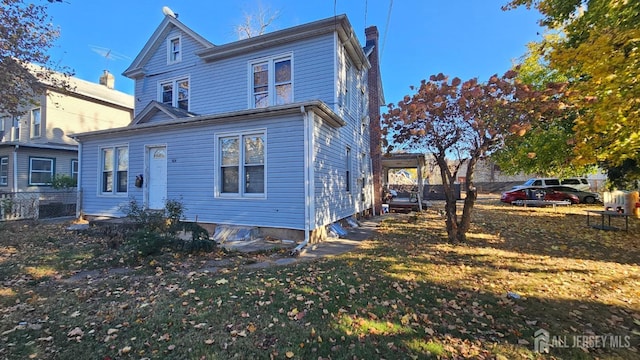 rear view of property with a chimney, fence, and a lawn