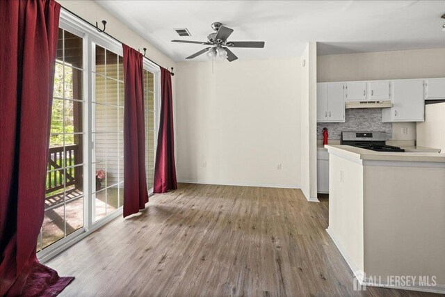 kitchen with stainless steel gas stove, light wood-style floors, baseboards, decorative backsplash, and under cabinet range hood