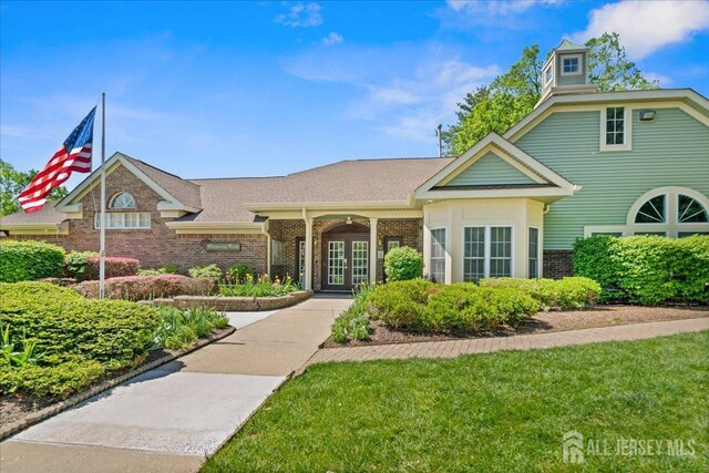 view of front of house with brick siding, roof with shingles, french doors, and a front yard