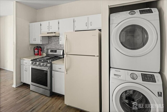 kitchen with stainless steel gas range oven, light countertops, freestanding refrigerator, under cabinet range hood, and stacked washer and clothes dryer
