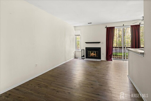 unfurnished living room featuring a fireplace with flush hearth, baseboards, dark wood-style floors, and visible vents