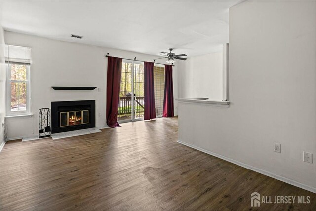 unfurnished living room featuring baseboards, visible vents, a fireplace with flush hearth, and wood finished floors