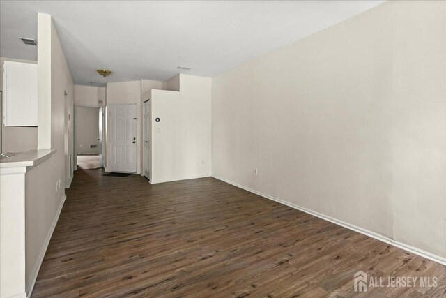 unfurnished room with baseboards, dark wood-style flooring, and visible vents
