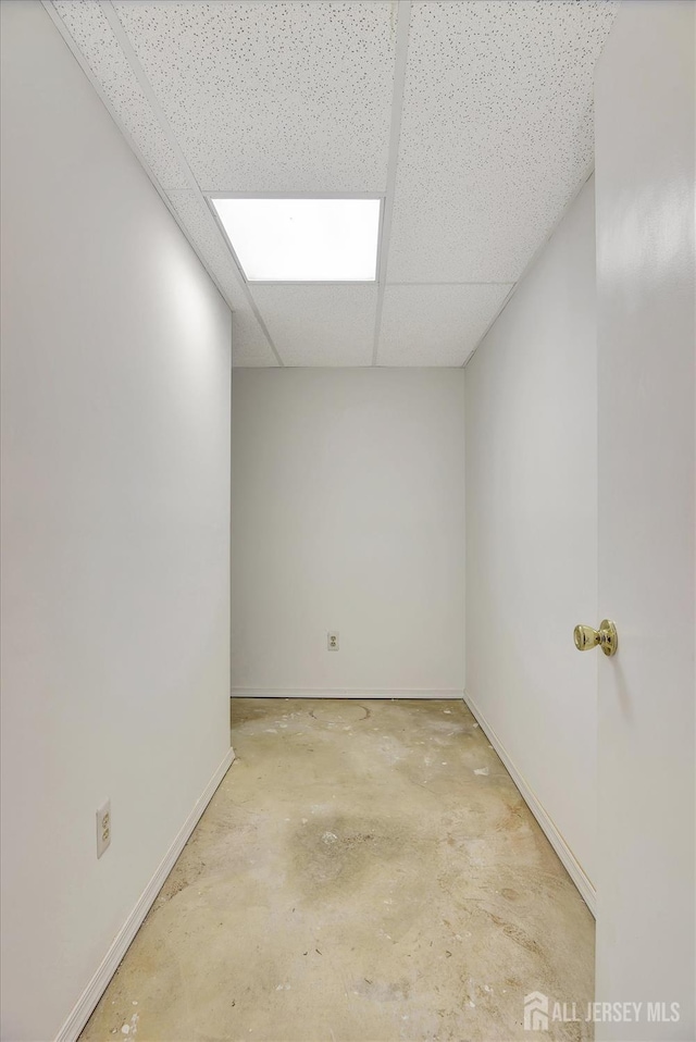 empty room featuring a drop ceiling, concrete floors, and baseboards