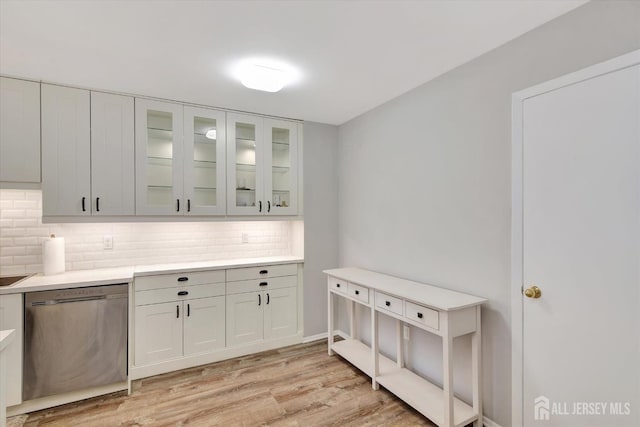 kitchen with light wood-style flooring, white cabinets, glass insert cabinets, stainless steel dishwasher, and tasteful backsplash