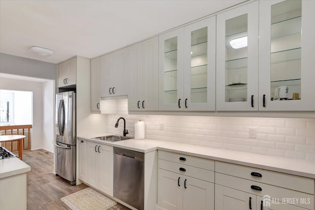 kitchen with a sink, decorative backsplash, light countertops, appliances with stainless steel finishes, and light wood-type flooring