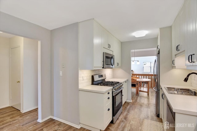 kitchen featuring backsplash, light countertops, light wood-style floors, stainless steel appliances, and a sink