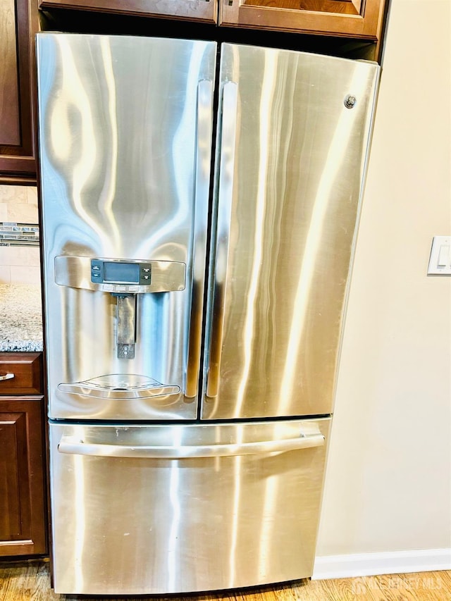 kitchen view of stainless steel fridge, light stone countertops, baseboards, and light wood finished floors
