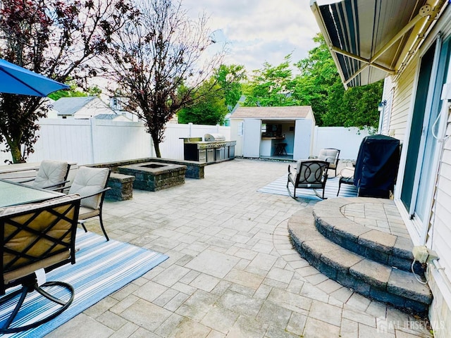 view of patio featuring a fenced backyard, an outdoor kitchen, an outdoor structure, and a storage unit