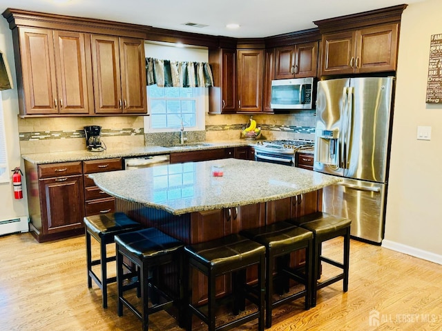 kitchen featuring stainless steel appliances, a sink, a kitchen bar, light wood-style floors, and tasteful backsplash
