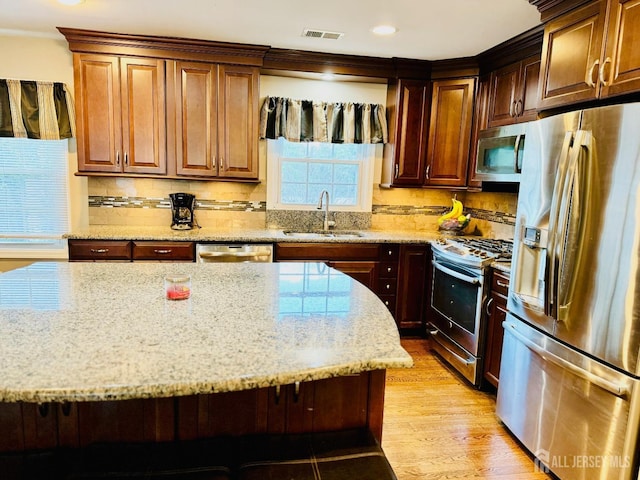 kitchen with stainless steel appliances, a sink, light stone counters, backsplash, and light wood-style flooring